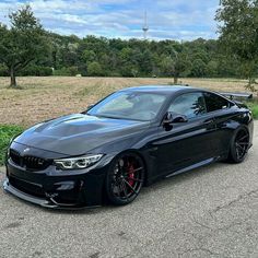 a black car parked on the side of a road next to some grass and trees