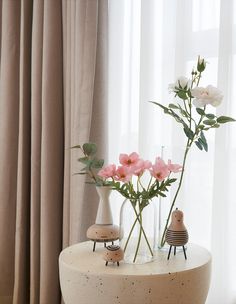 two vases with flowers in them sitting on a table next to a curtained window