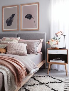 a bed with pink pillows and blankets on top of it next to a nightstand in front of a window