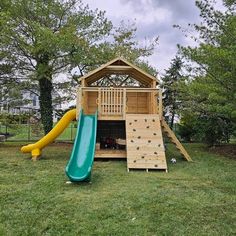 a wooden playset with a slide and climbing wall in the back yard, surrounded by trees