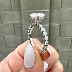 a woman's hand holding a diamond ring in front of a brick wall background