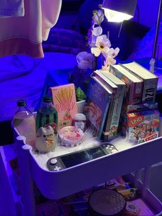 a white table topped with lots of books next to a purple light filled bedroom bed