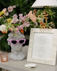 a vase with flowers in it next to a sign and a glass on a table