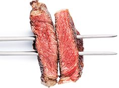 two steaks on skewers being held by tongs against a white background