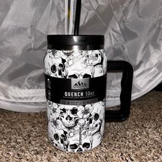 a black and white coffee mug with skulls on it sitting in front of a curtain