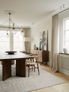 a dining room table and chairs in front of two large windows with drapes on them