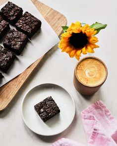 some brownies are on a plate next to a cup of coffee and a sunflower