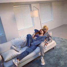 two people are laying on a couch in a living room with white walls and blue carpet