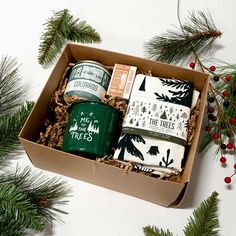 a christmas gift box filled with tea, coffee cups and napkins next to pine branches