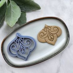 two cookie cutters sitting on top of a white plate next to a green plant