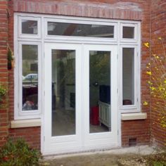 an open patio door in front of a brick building with white windows and glass doors