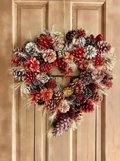 a wreath made out of pine cones is hanging on the front door with red and white flowers