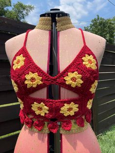 the back of a dress with crocheted flowers on it, sitting in front of a fence