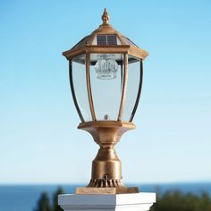 an old fashioned light on top of a white post by the ocean with blue skies in the background