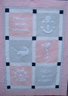 a pink and gray quilt with white embroidered words on the front, along with an anchor