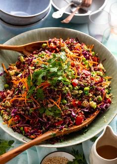 a salad in a bowl with wooden spoons on a table next to other dishes