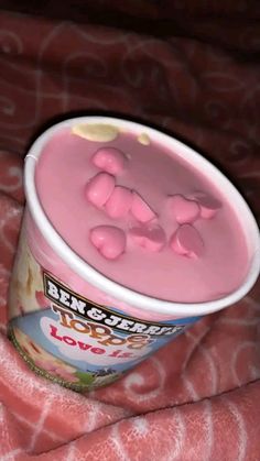 a pink yogurt with gummy bears in it sitting on a bed next to a blanket