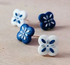 three blue and white flower shaped studs sitting on top of a wooden table next to each other