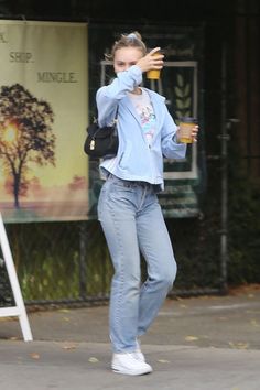 a woman standing on the sidewalk drinking from a bottle and holding her hand up to her face