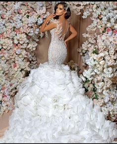 a woman in a white wedding dress standing next to a flower covered wall with flowers on it