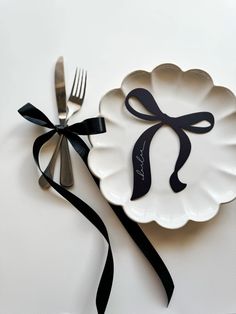 a white plate topped with a black bow next to a fork and knife