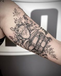 a woman's arm with an old fashioned book and roses tattoo on the arm