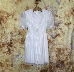 "A girl's size 8 lacy white short sleeve dress for first communion, flower girl or special occasion. The dress is below knee length with a back tie and lace hem and trim at the sleeves. It has a basque waist with lace, satin rosette and string of faux pearls at the bodice. The  label reads, \"Bonnie Jean New York\".  It measures 28\" around the chest, the wast is 23\" and the length is 30\". Excellent condition. Hand or gentle machine wash. Size 8. Catalog # 8703" Spring Lace Baptism Dress With Lace Collar, Short Sleeve Dress With Fitted Bodice For Confirmation, Spring Baptism Dress With Lace Sleeves, Spring Baptism Dress With Lace Collar, Elegant Short Sleeve First Communion Dress With Fitted Bodice, Elegant Short Sleeve First Communion Summer Dress, Elegant First Communion Dress With Fitted Bodice, Elegant First Communion Dress With Short Sleeves, Short Sleeve Lace Dress For Confirmation