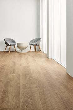 two chairs sitting on top of a wooden floor next to a white vase and window