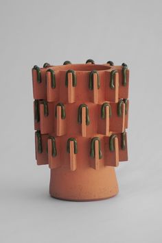 an orange vase with green spikes on the top and bottom, in front of a gray background