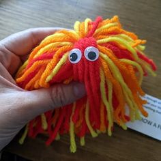 a hand holding a small orange and yellow stuffed animal with long dreadlocks on it's head