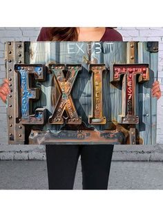 a woman holding up a sign that says exit and the word fix spelled in metal letters