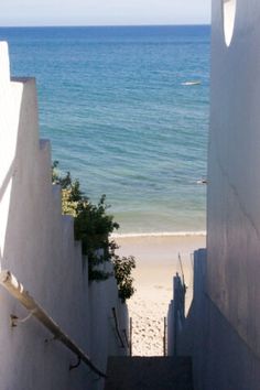 an alley way leading to the beach with stairs going up and down into the water