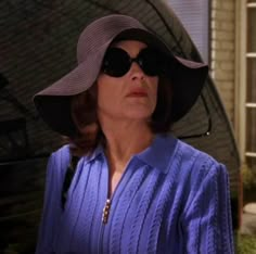 a woman wearing a hat and sunglasses standing in front of a house