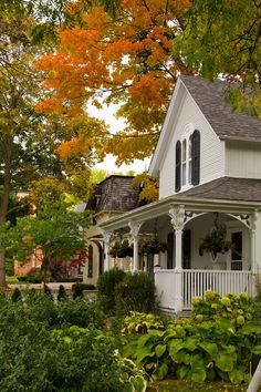 a white house surrounded by trees and bushes in the fall with leaves turning to yellow