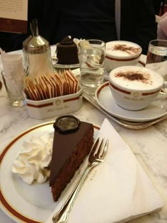 a slice of chocolate cake on a plate with whipped cream and other desserts around it