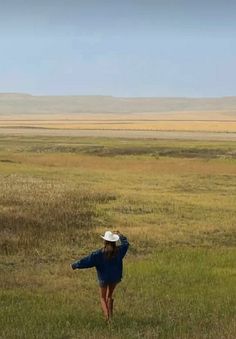 a woman in a blue dress and hat flying a kite on the open plain with mountains in the background