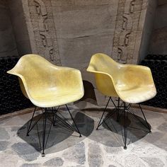 two yellow chairs sitting next to each other on top of a stone floor in front of a wall