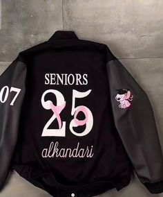 the back of a black jacket with pink and white numbers on it, sitting against a wall