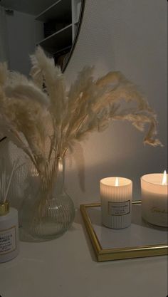 two candles are on a table next to a vase with feathers in it and a mirror behind them