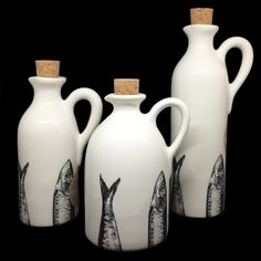 three white vases with fish painted on them are lined up against a black background