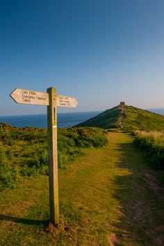 a wooden sign pointing in opposite directions on a grassy hill overlooking the ocean and cliffs