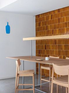 a wooden table with chairs and a blue vase on the wall in front of it