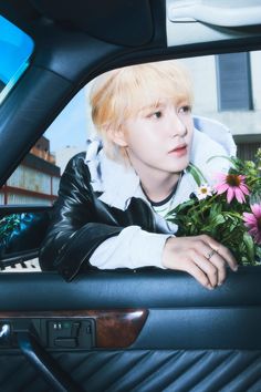 a young man sitting in the back seat of a car holding flowers and looking out the window