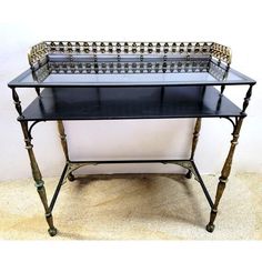 a black and gold metal table with two shelves on each side, sitting against a white wall