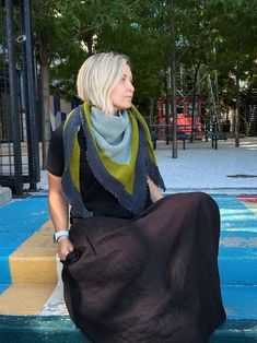 a woman sitting on the ground wearing a black dress and green scarf over her shoulders