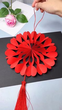 a hand holding a red paper flower on top of a table