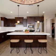 a large kitchen with wooden cabinets and white counter tops, along with bar stools