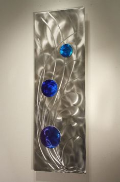 a metal wall hanging with three blue glass balls on it's side, in front of a white wall