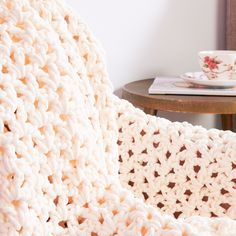 a white crocheted blanket sitting on top of a table next to a cup