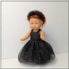 a doll with red hair wearing a black dress and headband, standing in front of a white wall